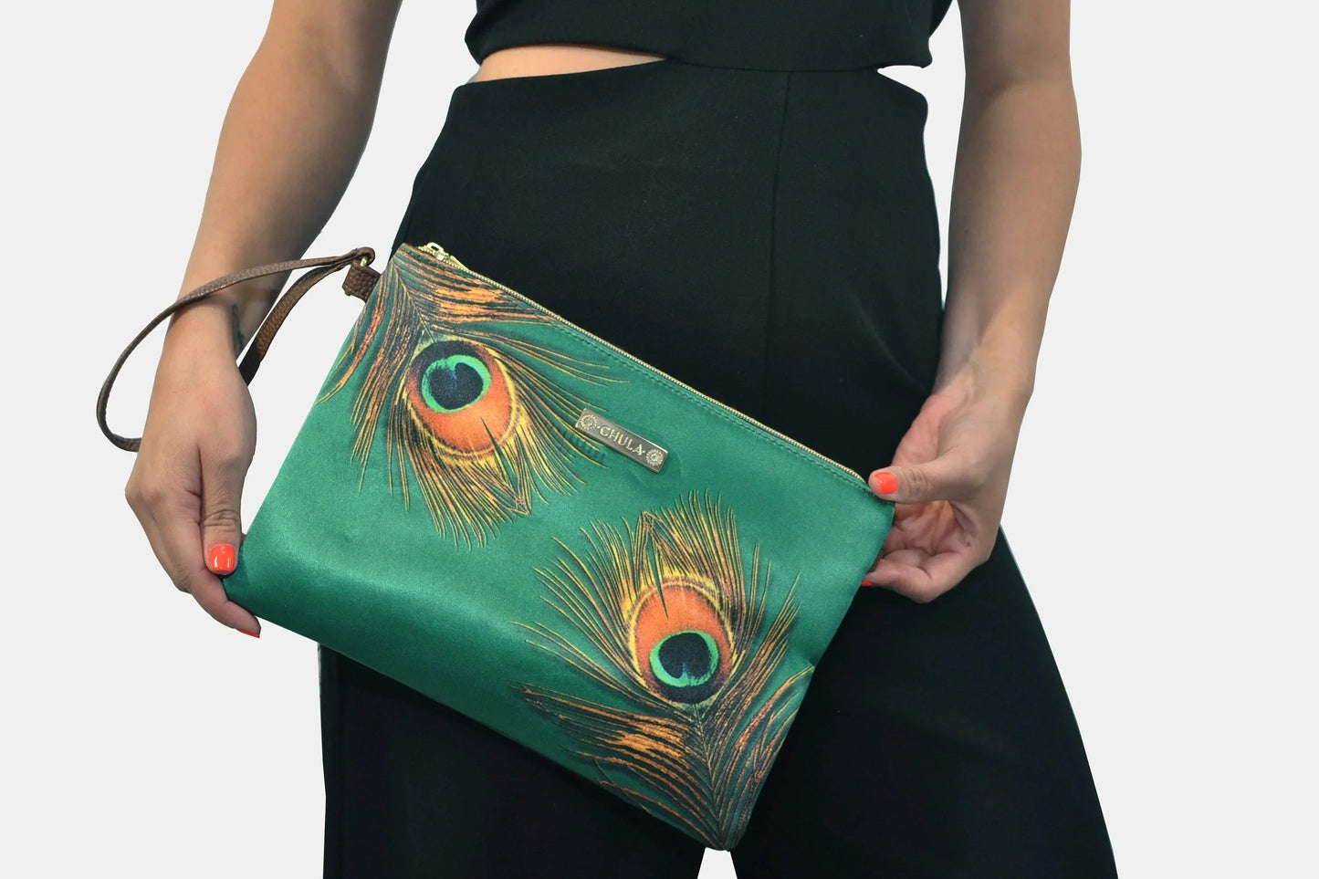 Bolso de mano pequeño tipo clutch verde con diseño de plumas de pavo real, sujetado por mujer.