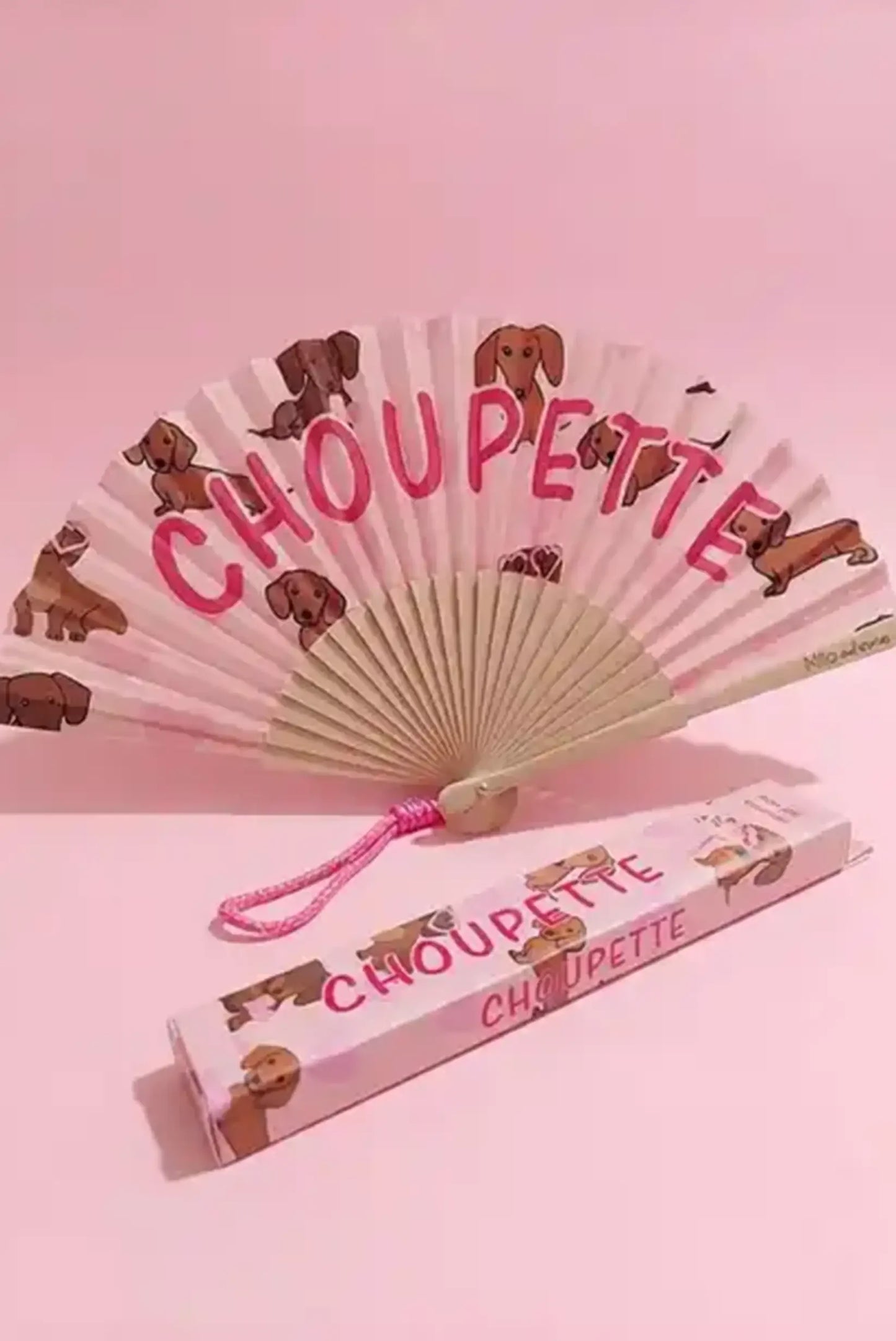 Abanico plegable con perros y texto 'CHOUPEETTE', ideal como complemento de moda femenina en tonos rosas.