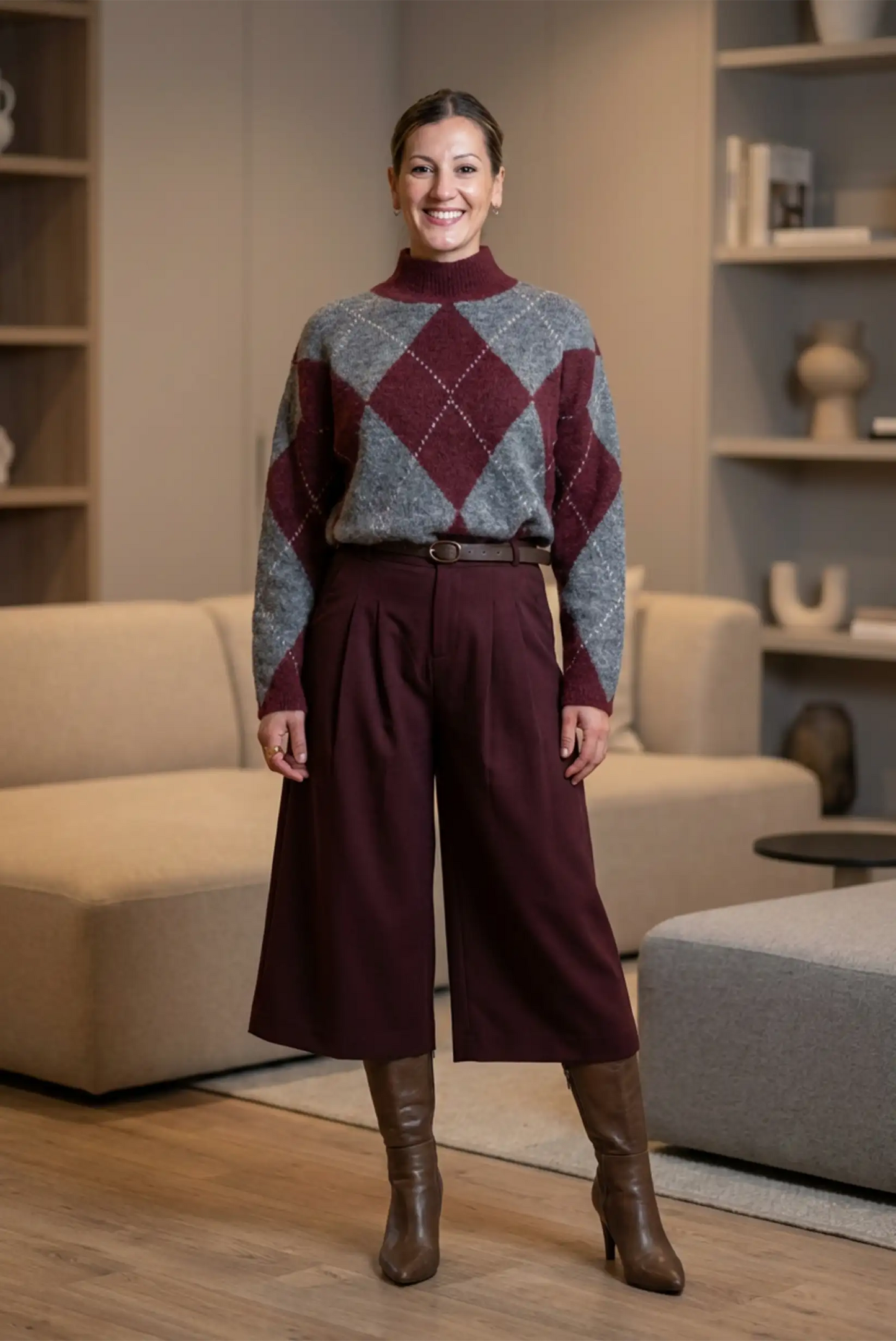Mujer con suéter gris y burdeos de rombos y bermuda larga burdeos, botas marrones en sala moderna