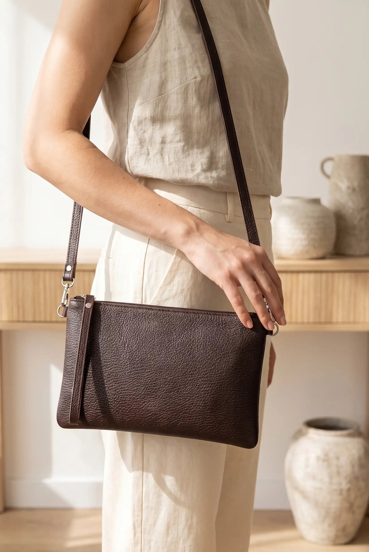 Mujer vistiendo ropa de lino clara y llevando un bolso clutch de piel marrón chocolate de CHICA del Sur