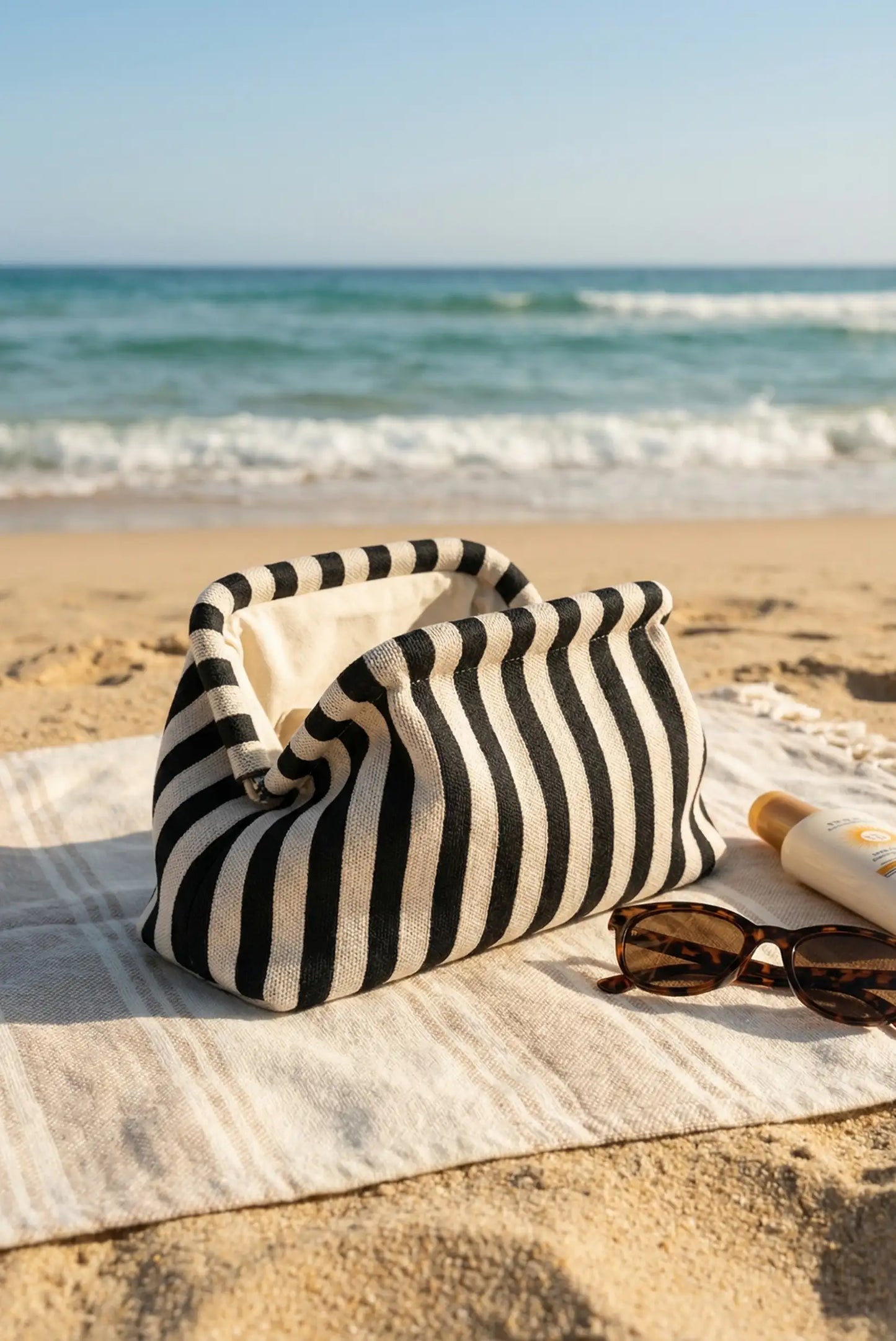 Bolso clutch neceser de rayas blanco y negro sobre toalla en la playa