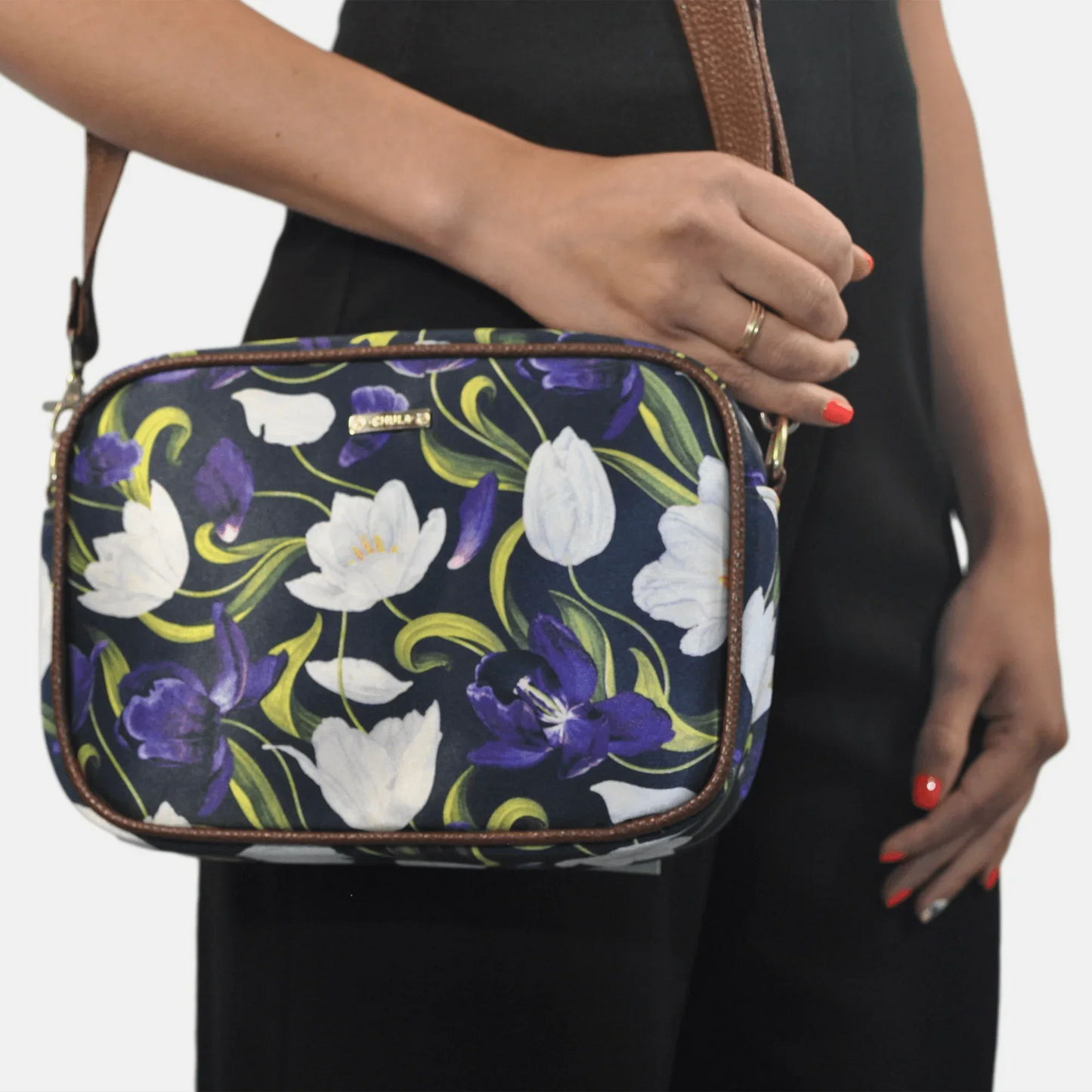 Bolso pequeño de mano y bandolera estampado de flores moradas y blancas, sobre fondo oscuro.