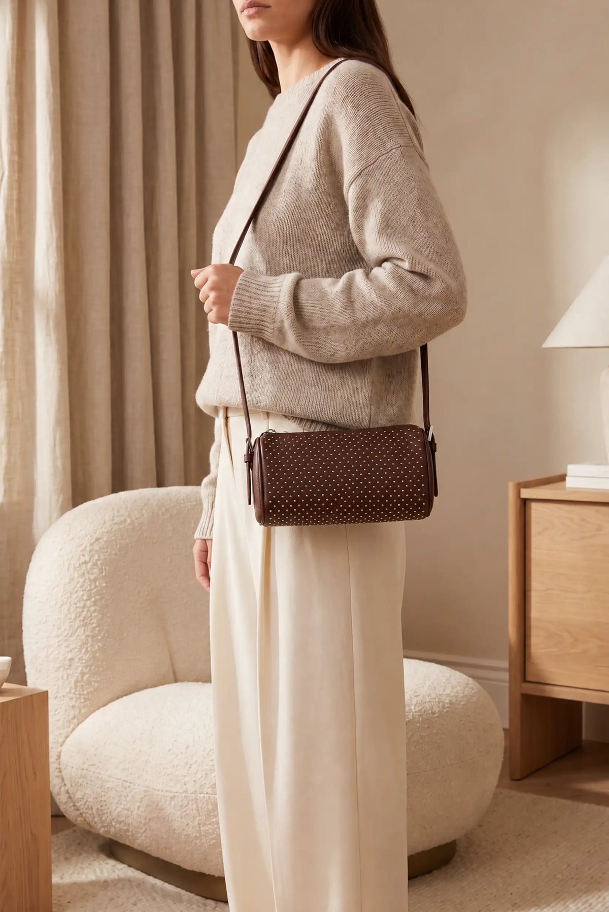 Mujer con jersey beige y bolso pequeño marrón de CHICA del Sur con tachuelas metálicas.