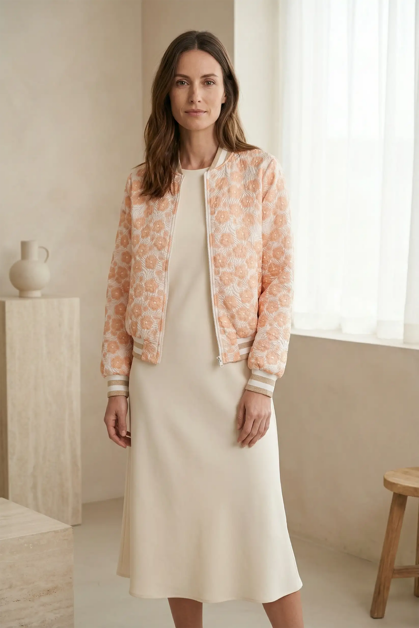 Mujer con chaqueta bomber de flores en tonos mandarina y vestido beige, moda primavera casual.
