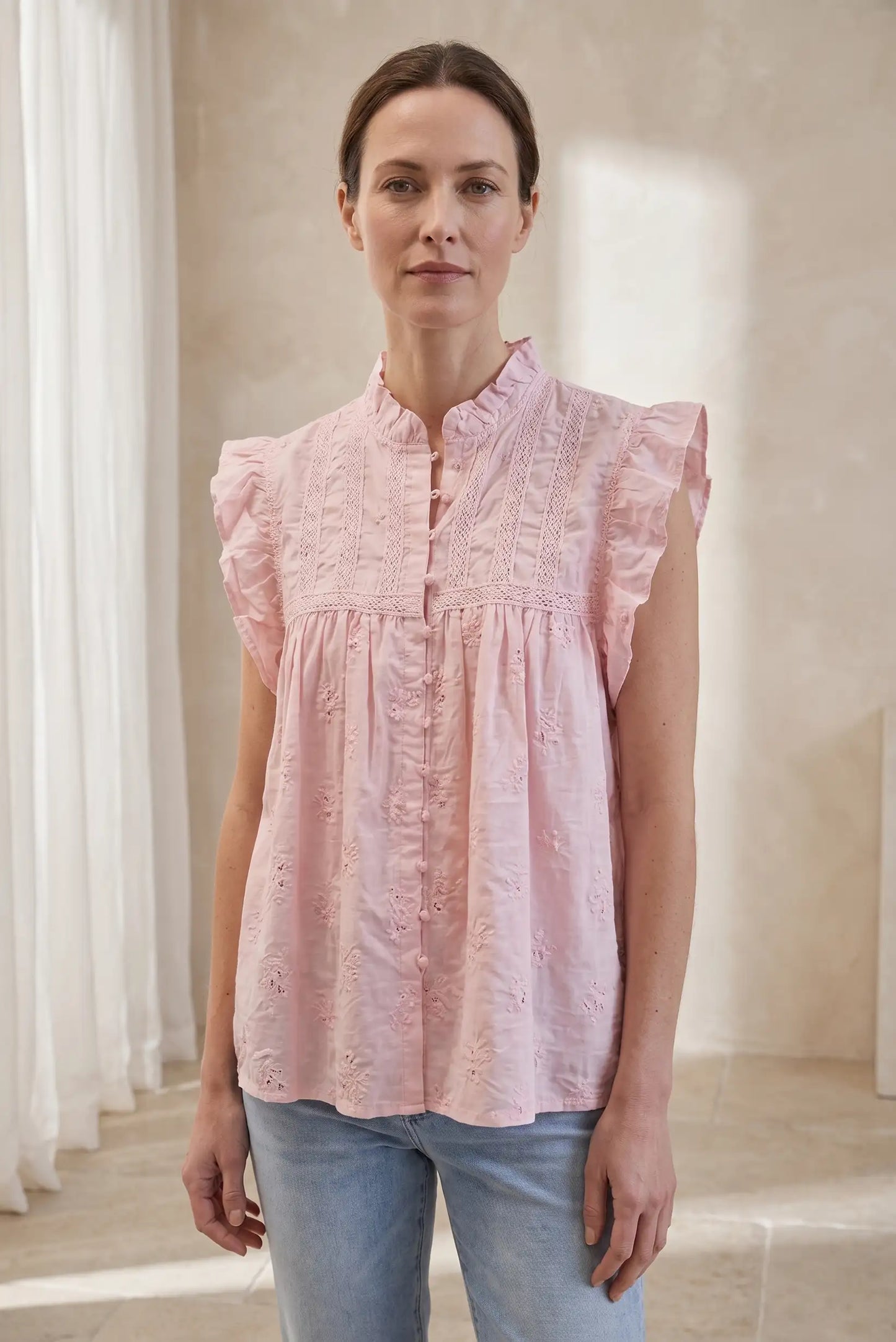 Mujer con blusa sin mangas rosa pastel, volantes y detalles bordados, look casual de verano.