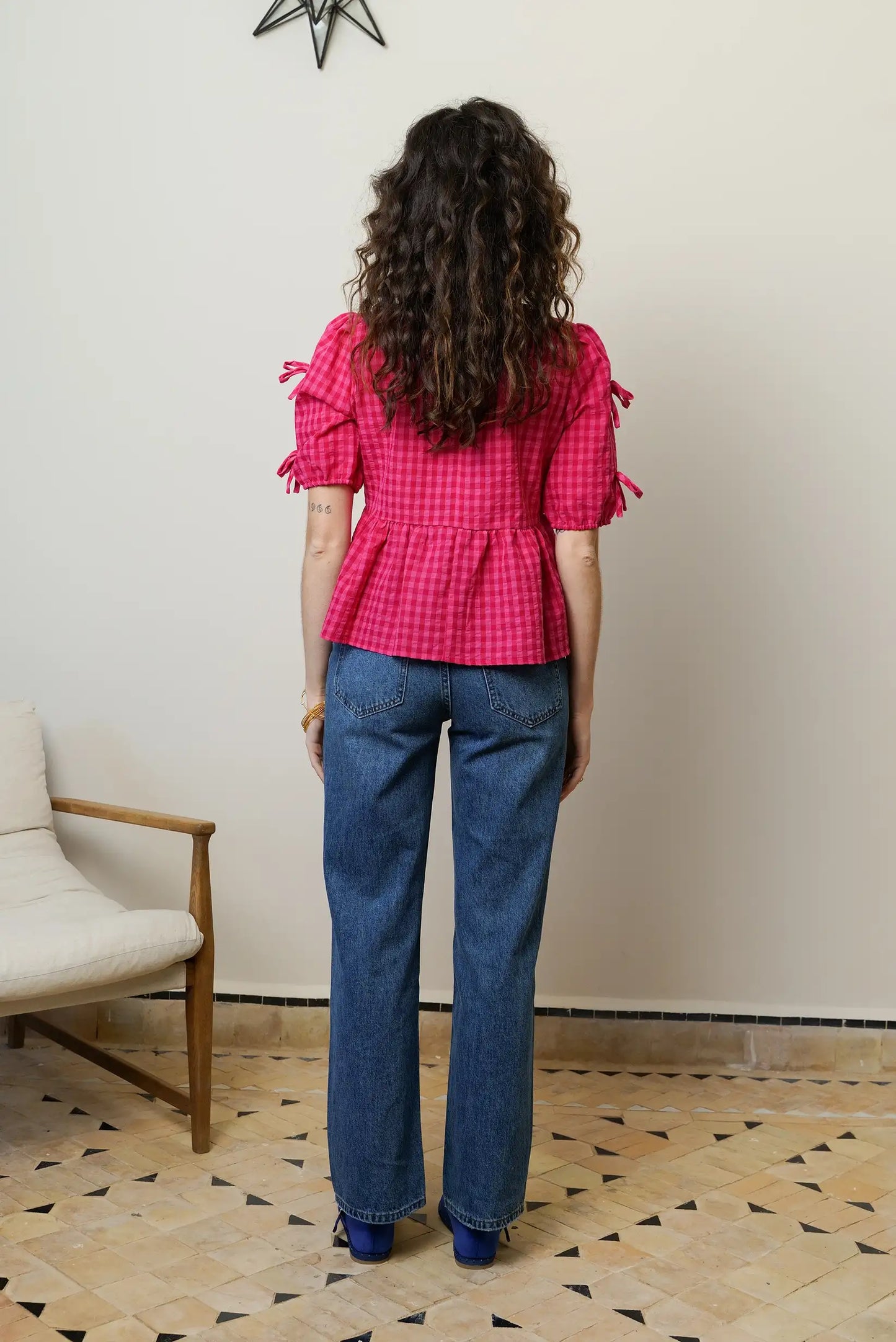 Mujer de espaldas con camisa rosa de cuadros y manga corta, pantalón vaquero recto.