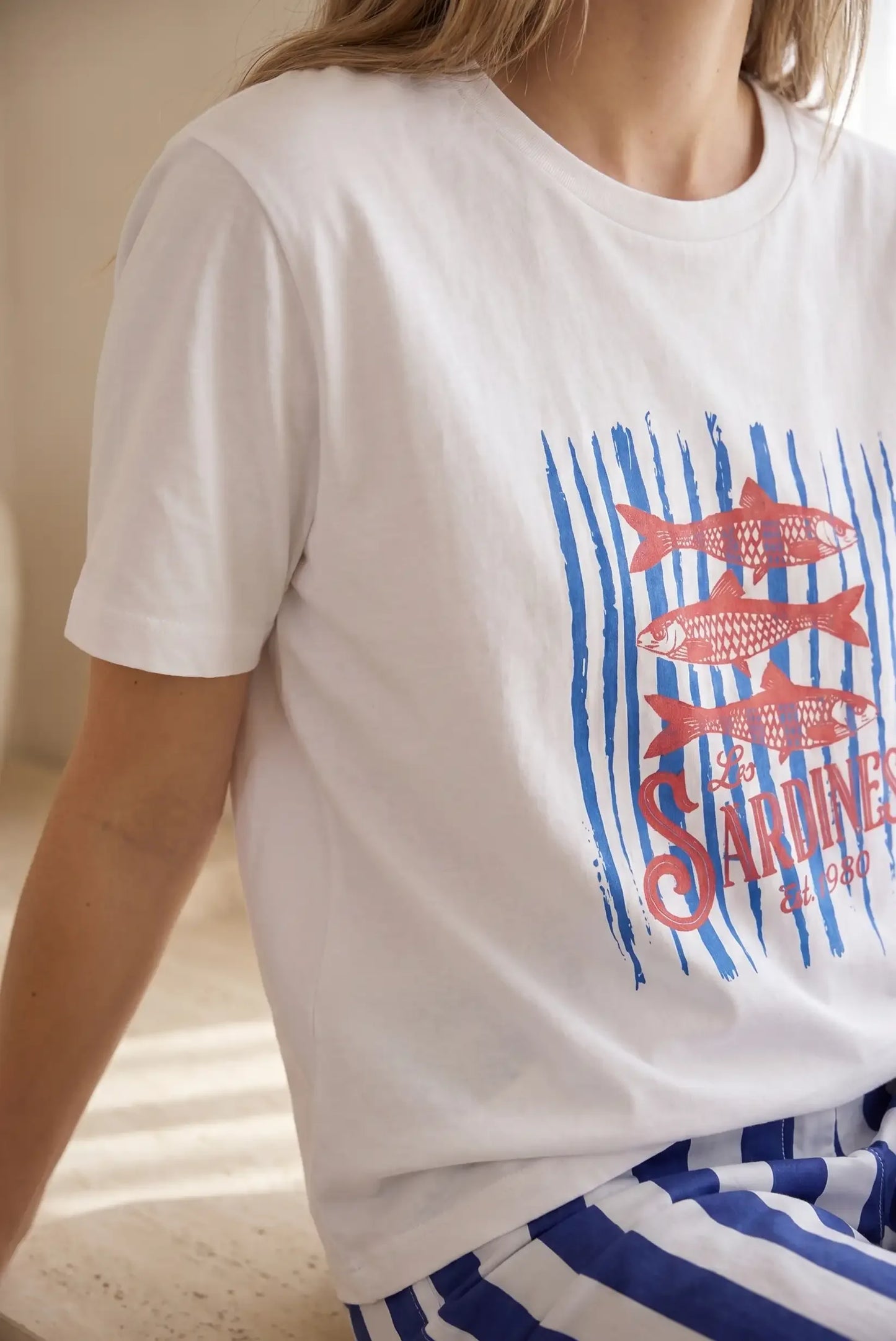 Camiseta blanca de mujer con manga corta, estampado de sardinas rojas y rayas azules.
