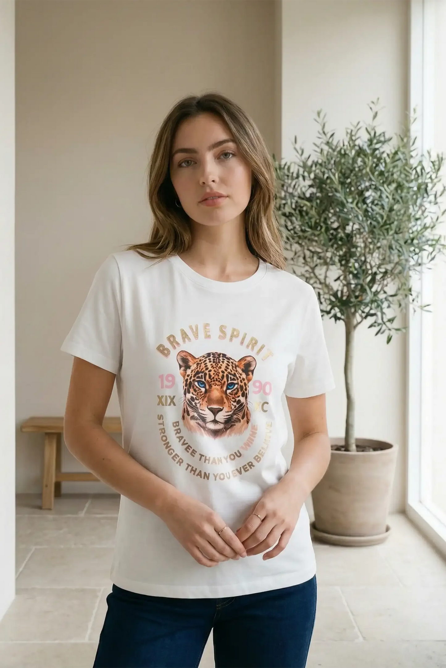 Mujer con camiseta blanca de manga corta con estampado de leopardo y texto dorado, estilo casual