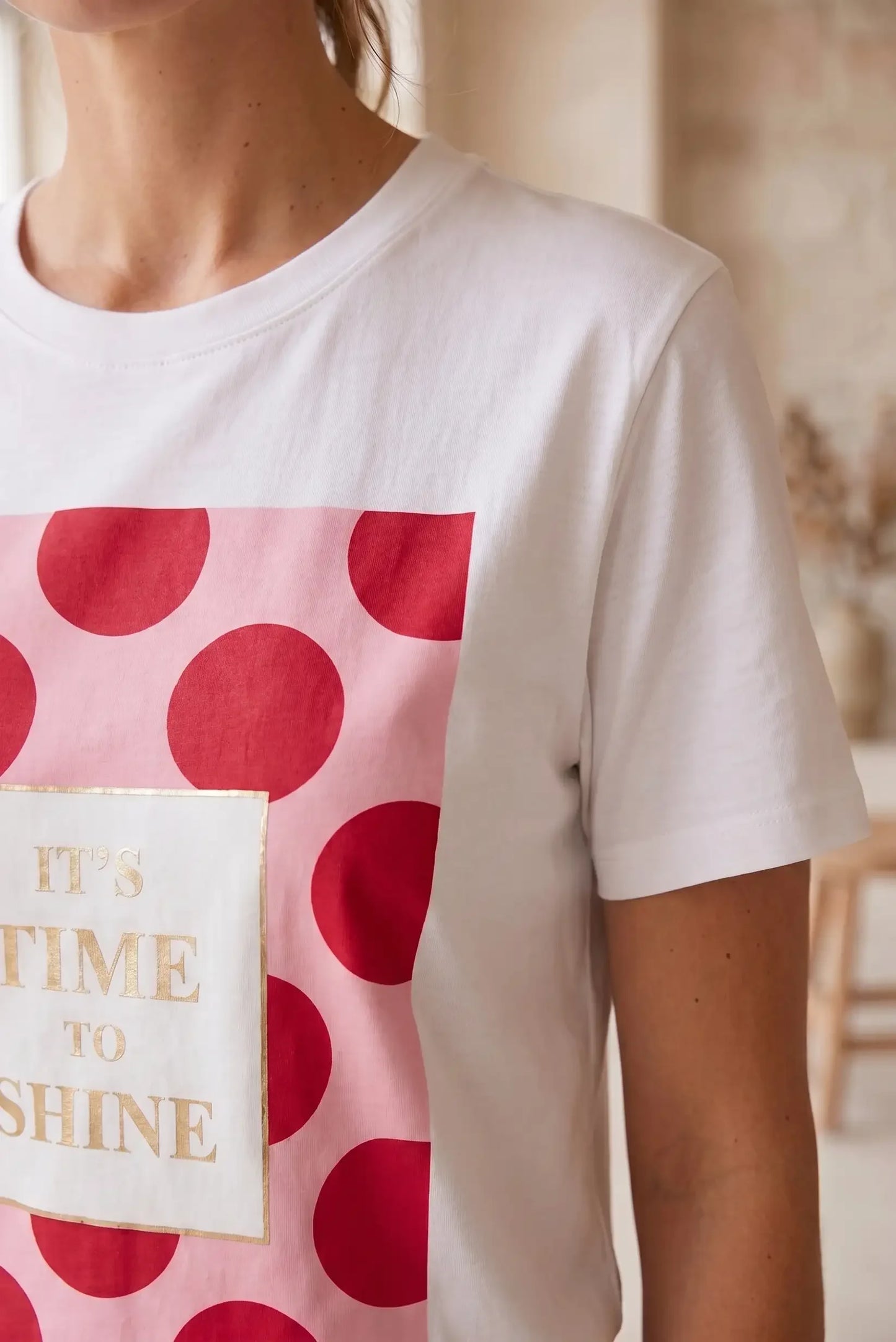 Camiseta blanca de mujer con manga corta, estampado de lunares rojos y mensaje dorado.
