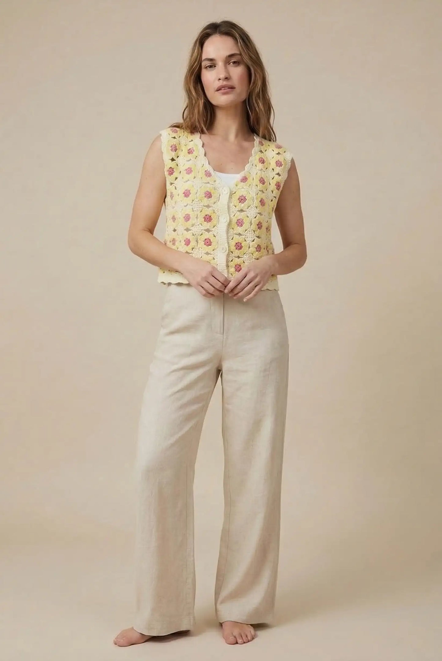Mujer con chaleco de crochet amarillo con flores pequeñas y pantalón beige, moda primavera
