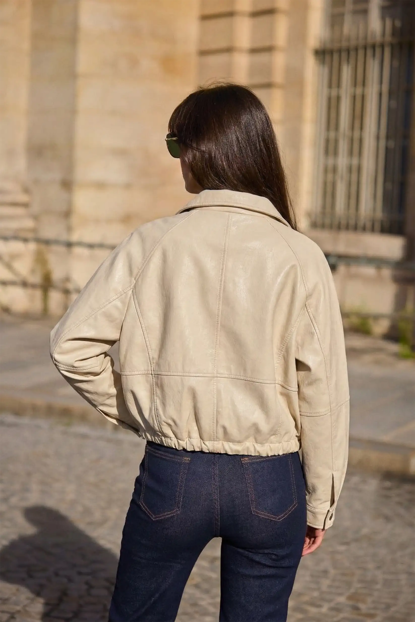 Mujer de espaldas con chaqueta polipiel beige claro y vaqueros azul oscuro en exterior