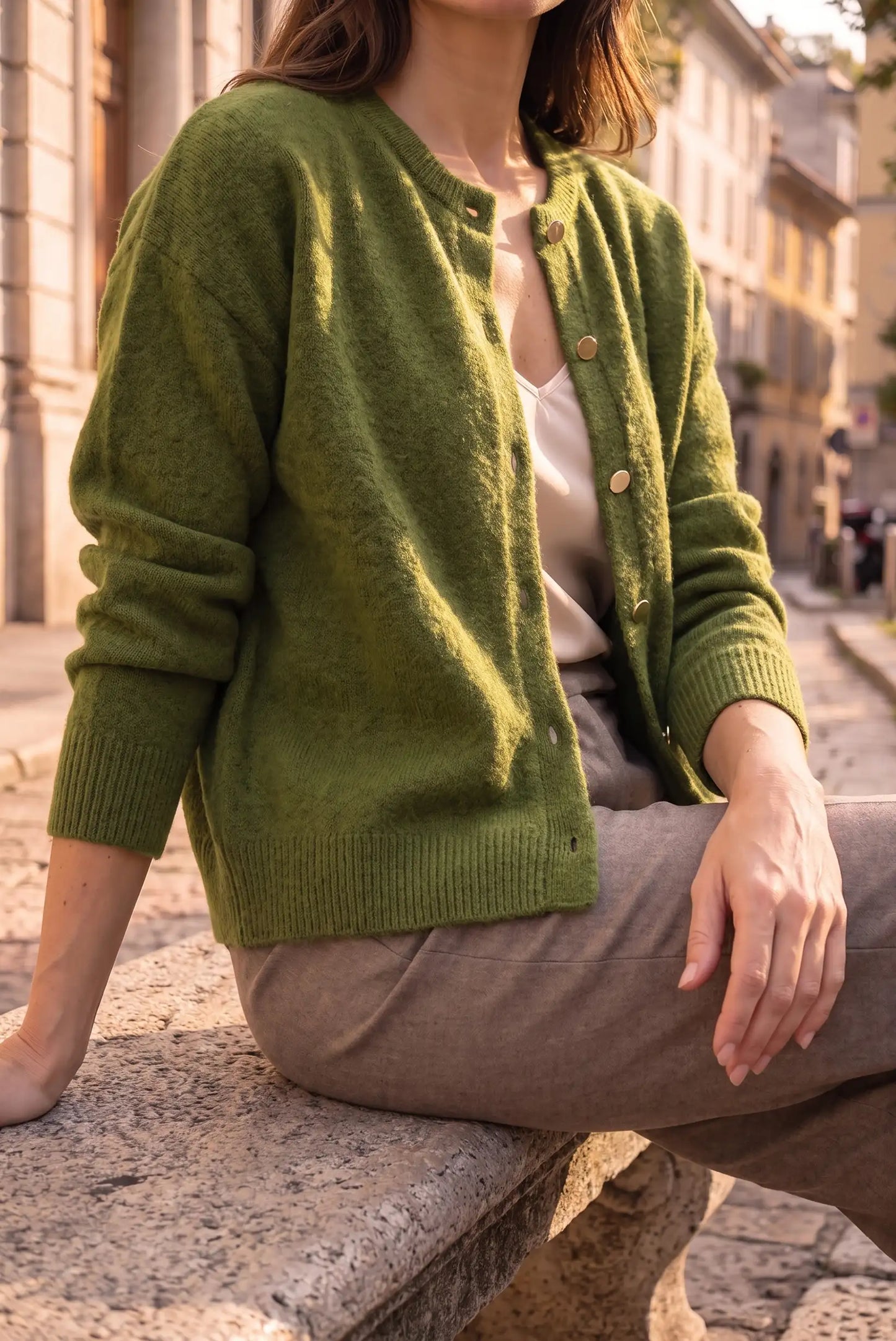 Mujer joven luciendo una rebeca de punto en color verde oliva y pantalones marrones.