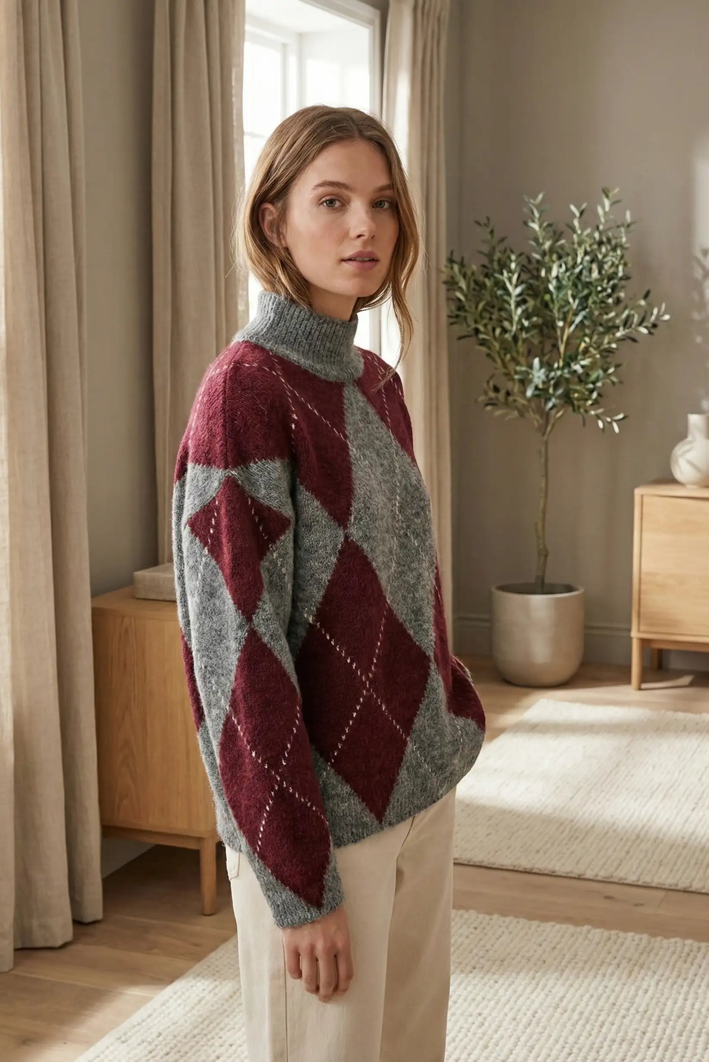 Mujer con jersey de rombos burdeos y gris de cuello alto en sala de estar moderna y luminosa