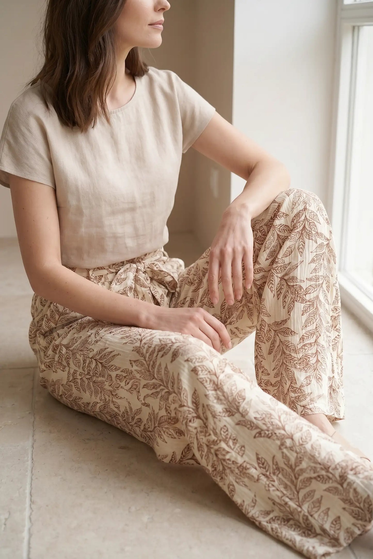 Mujer sentada con pantalón largo fluido beige estampado de hojas y blusa beige, look casual