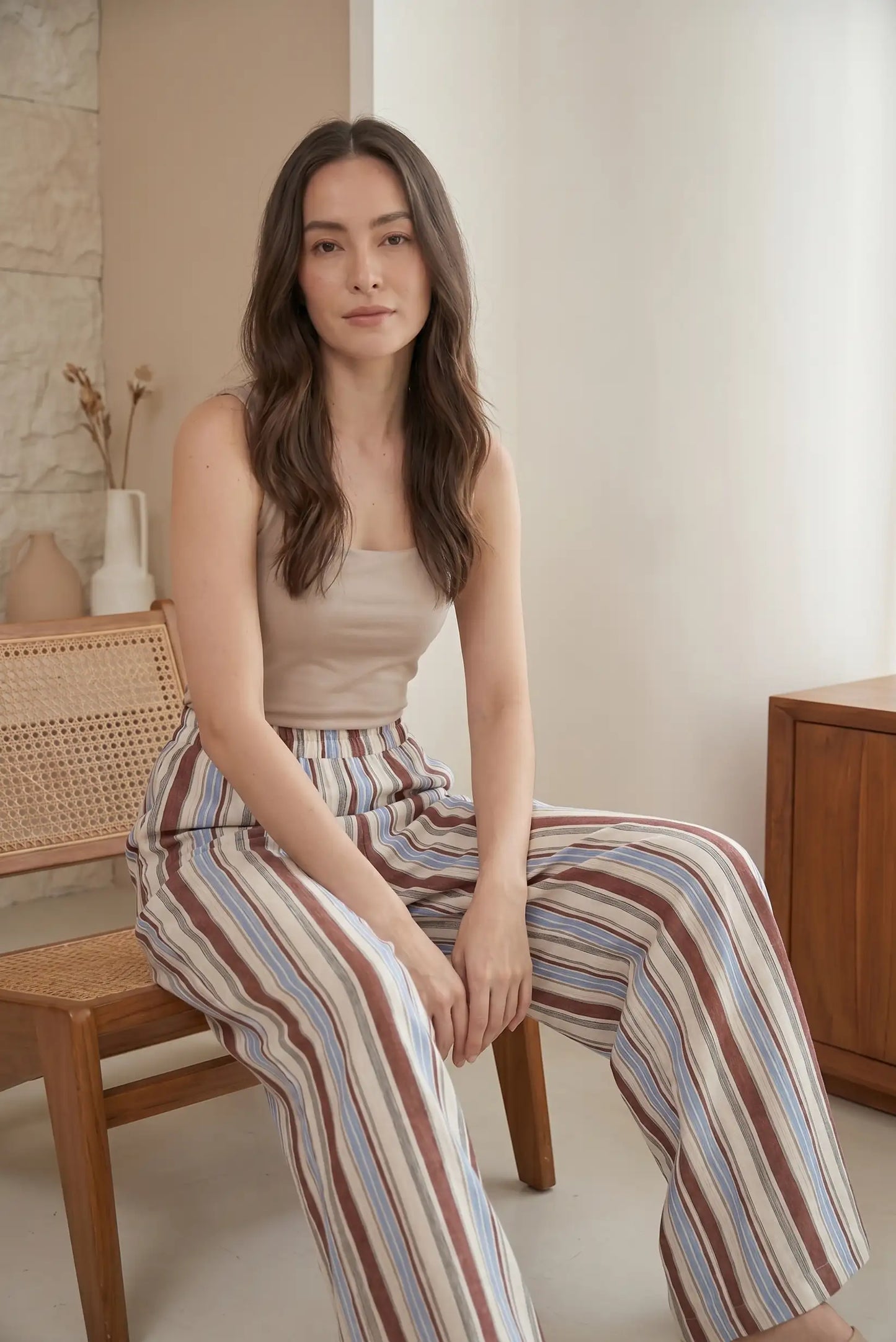Mujer con pantalón largo fluido de rayas azul y beige, sentada en ambiente minimalista