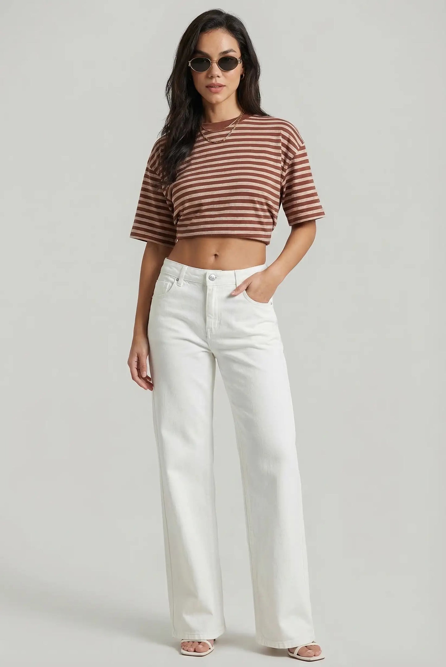 Mujer con pantalón vaquero blanco de pierna ancha y camiseta corta de rayas marrón