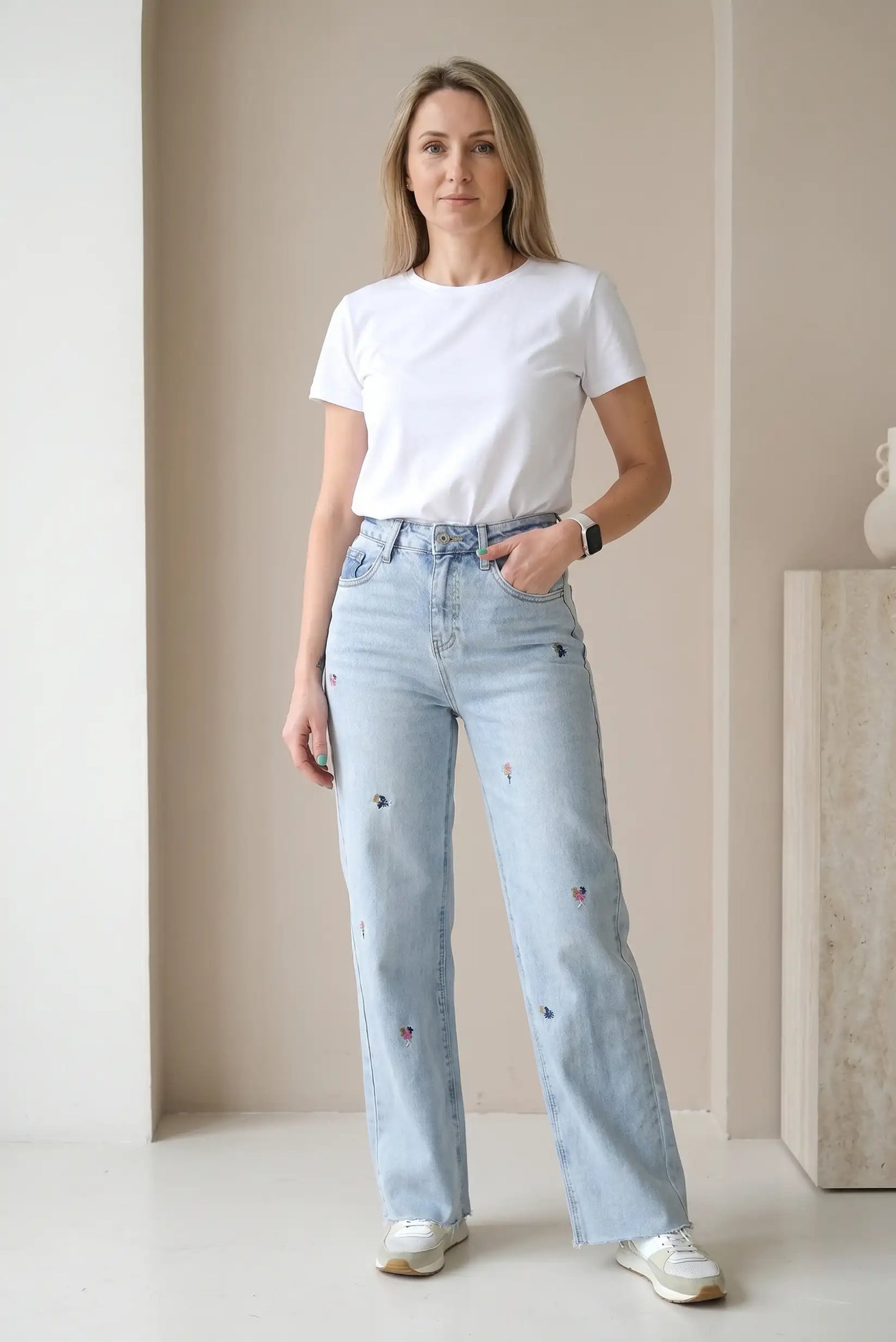 Mujer con camiseta blanca y pantalón vaquero largo azul claro con bordados de flores.