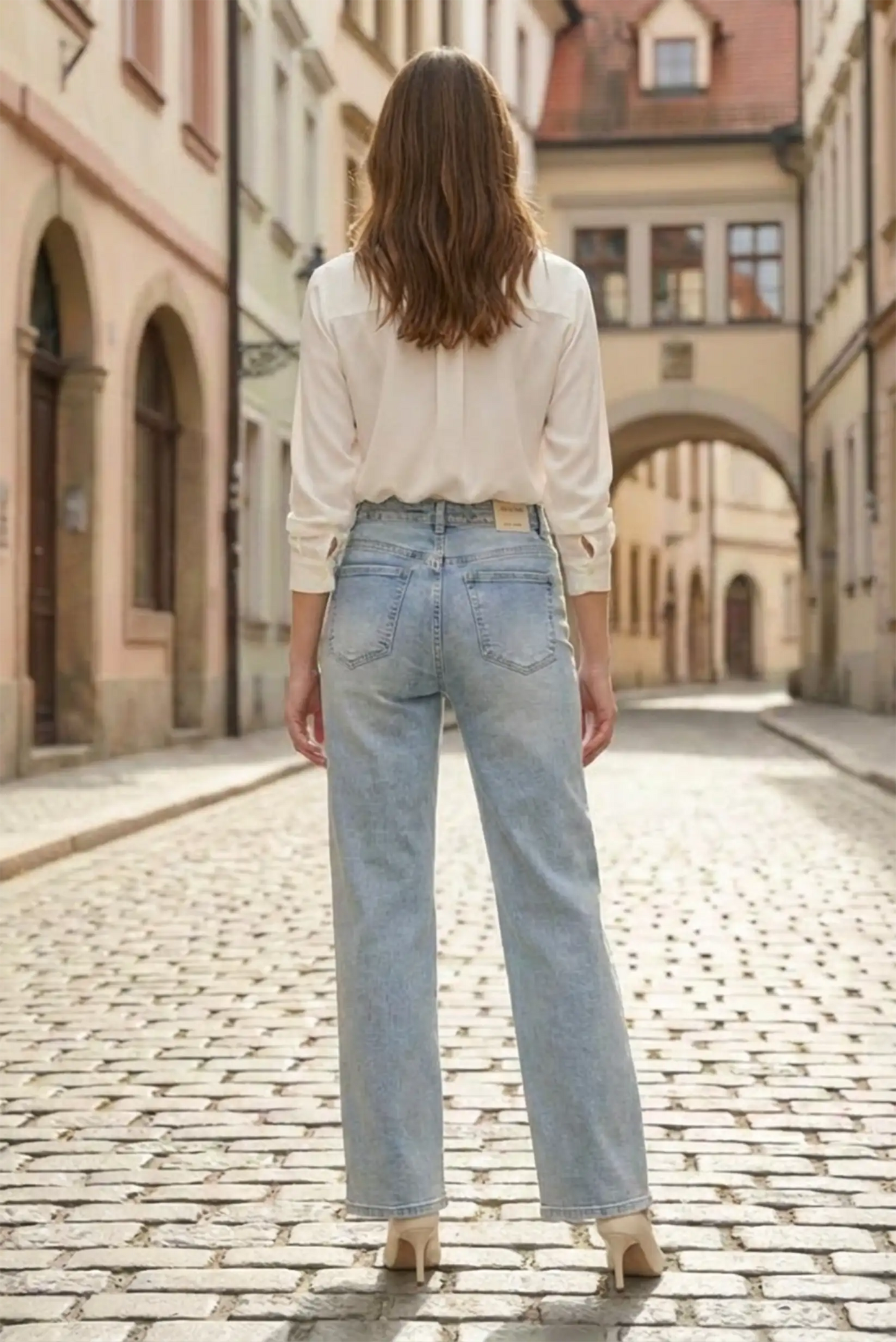Mujer con pantalón vaquero azul recto y blusa blanca en calle empedrada, moda CHICA del Sur