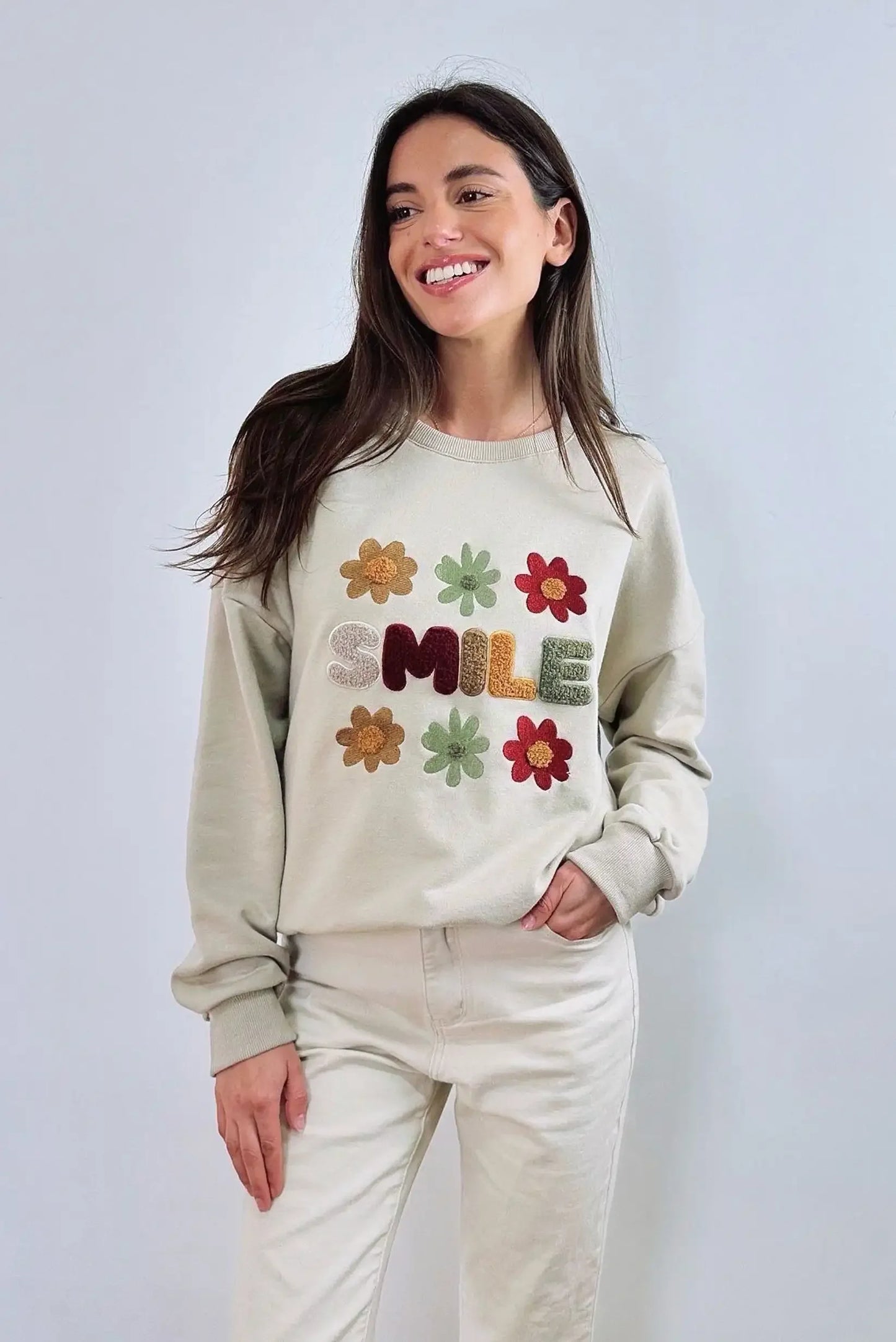 Mujer con sudadera beige de CHICA del Sur, bordada con flores de colores y la palabra SMILE.