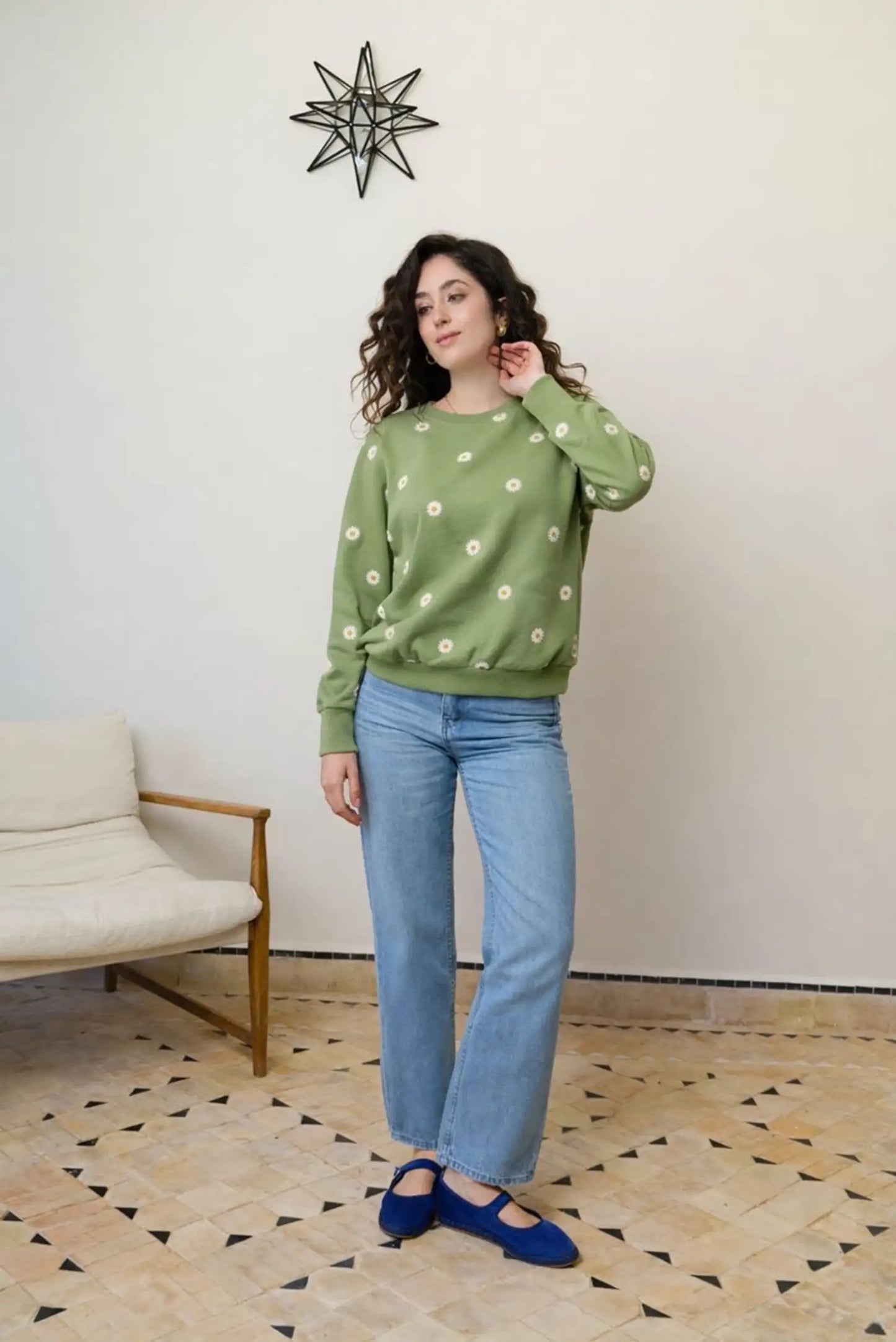 Mujer con sudadera verde de margaritas, jeans y zapatos azules en ambiente casual, moda CHICA del Sur