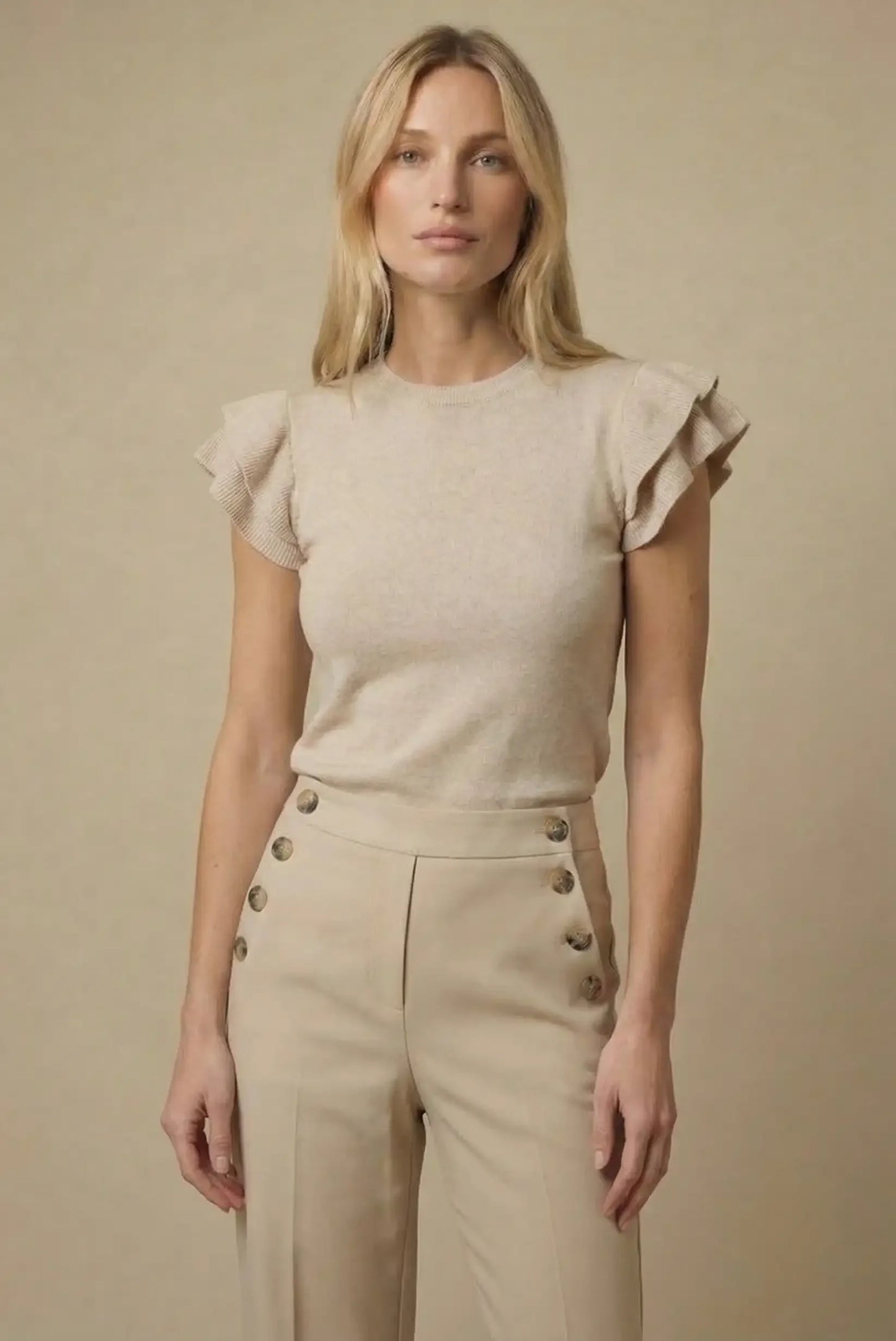 Mujer con top beige de manga corta con volantes y pantalón beige de botones, estilo casual.