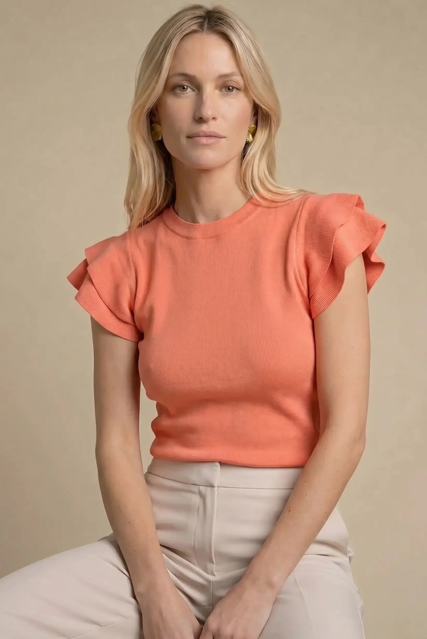 Mujer con top coral de manga corta con volantes, pantalón beige, fondo neutro