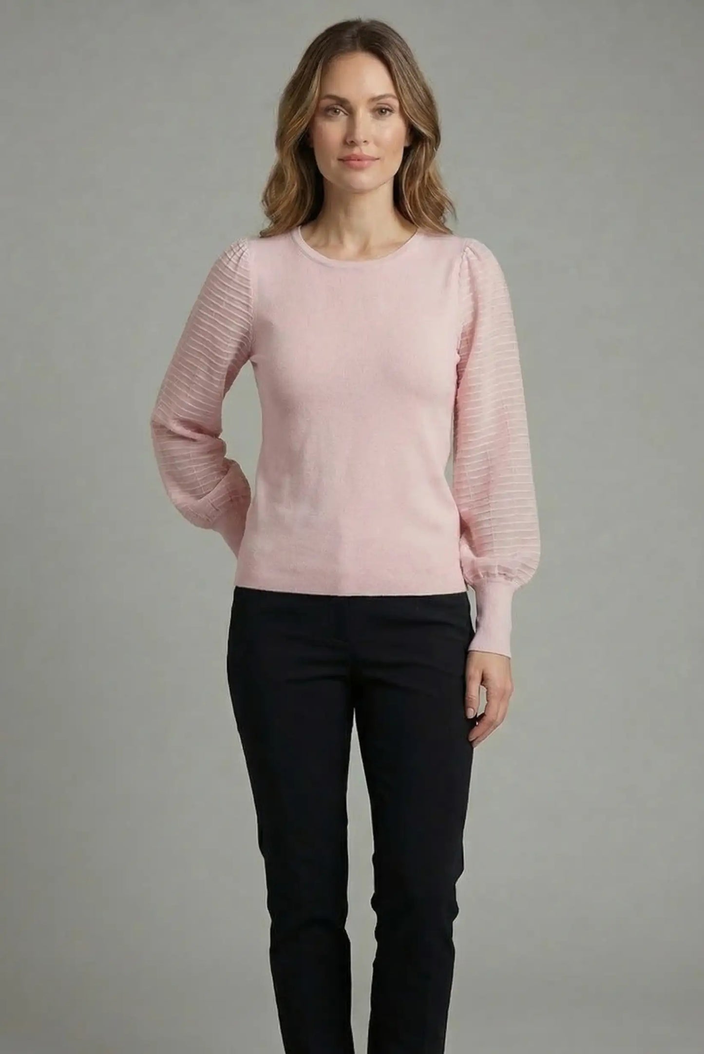 Mujer con top rosa pastel de manga larga abullonada y pantalón oscuro, moda casual femenina.