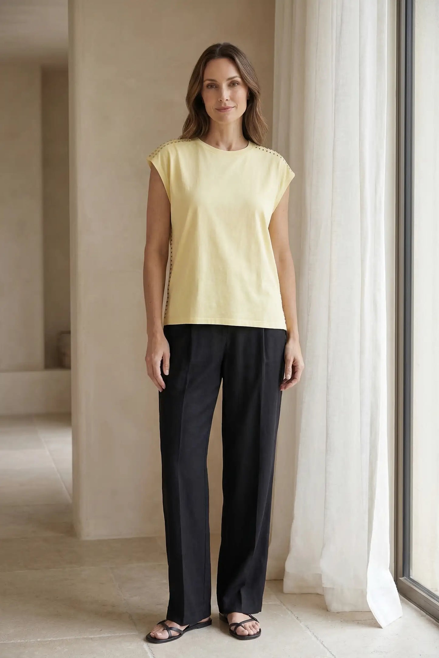Mujer con top amarillo sin mangas con tachuelas y pantalón negro, look casual moderno