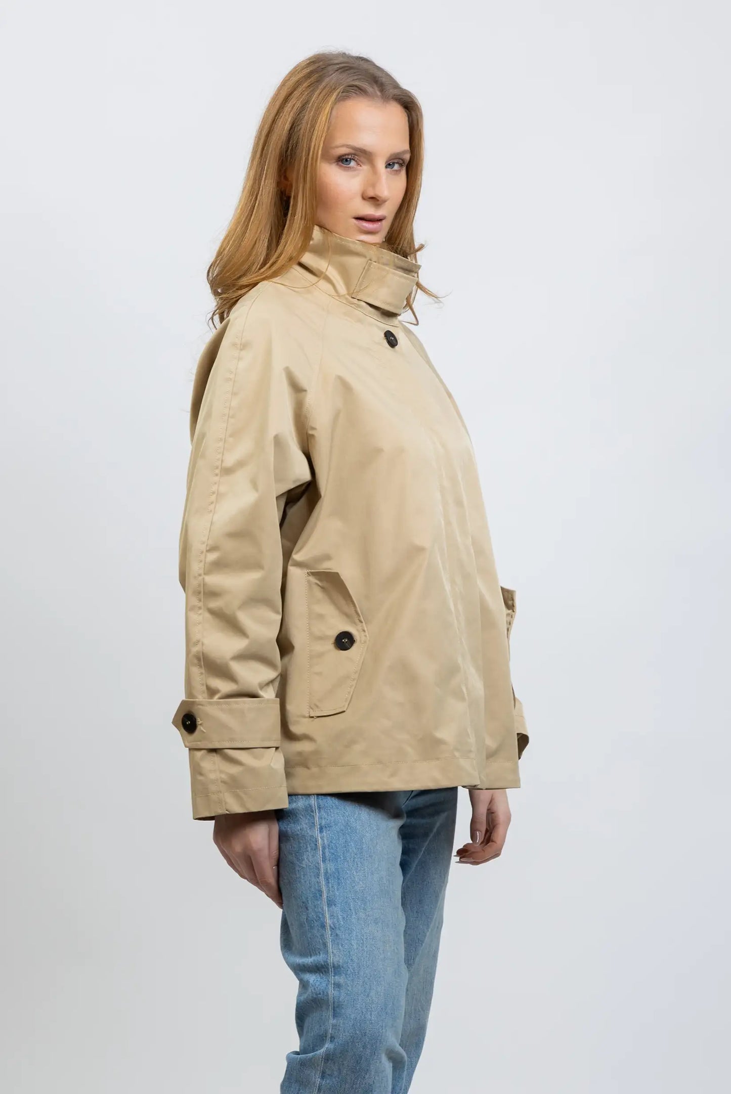 Mujer con cazadora trench beige de primavera y jeans claros, fondo blanco, moda casual.