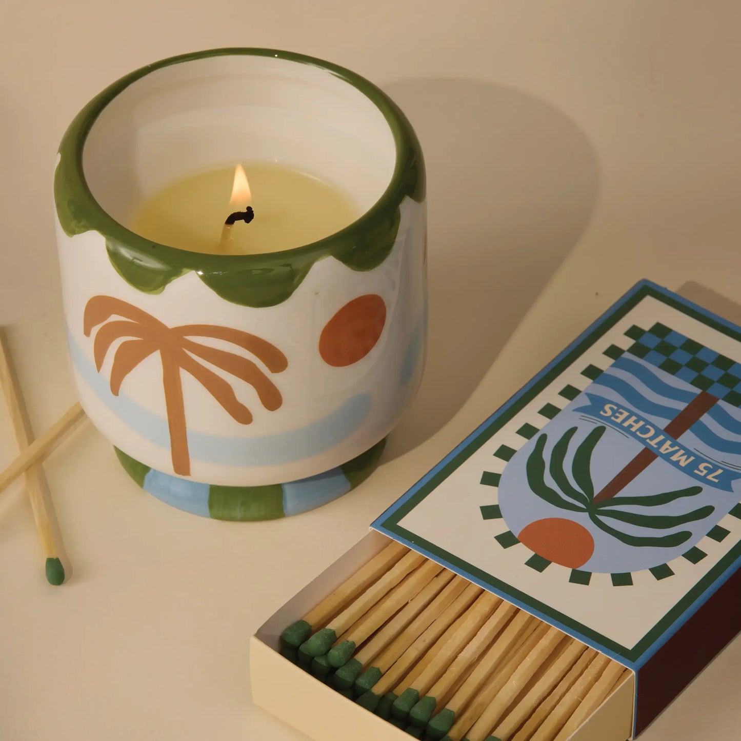 Vela aromática en vaso cerámico decorado con palmera junto a caja de cerillas, CHICA del Sur.
