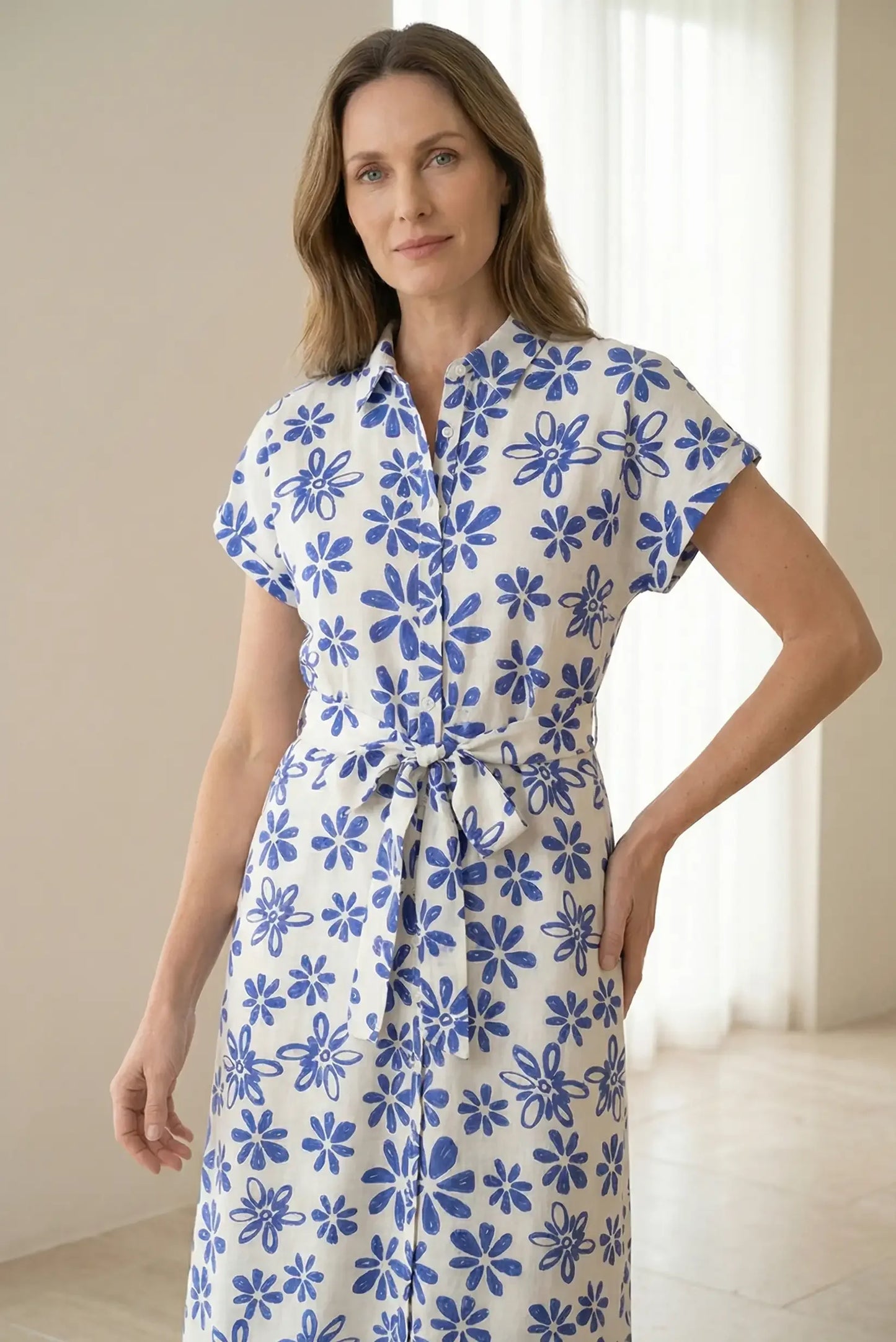 Mujer con vestido largo blanco de manga corta, estampado floral azul, cinturón anudado.