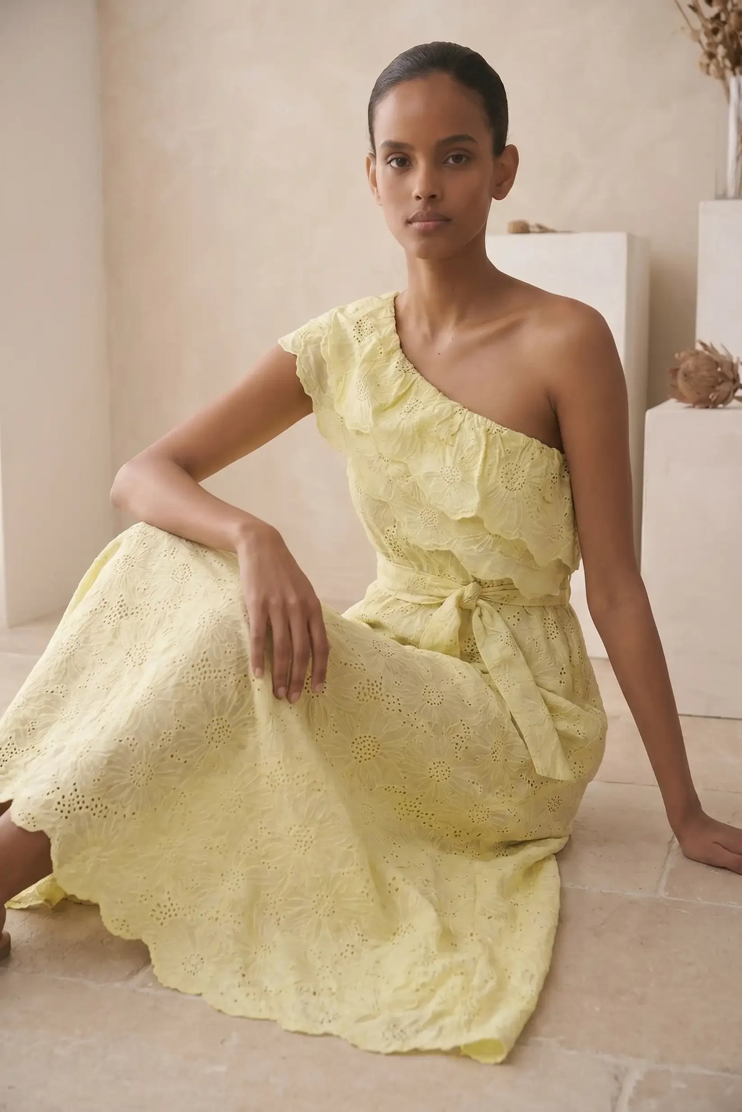 Mujer con vestido largo amarillo asimétrico de encaje, ideal para eventos de primavera.