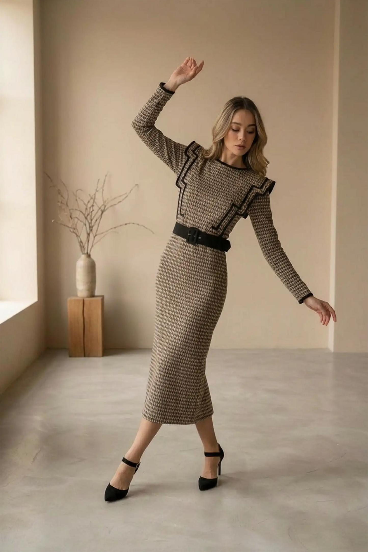 Mujer posando con vestido largo café clásico ajustado y zapatos negros de tacón en interiores minimalistas