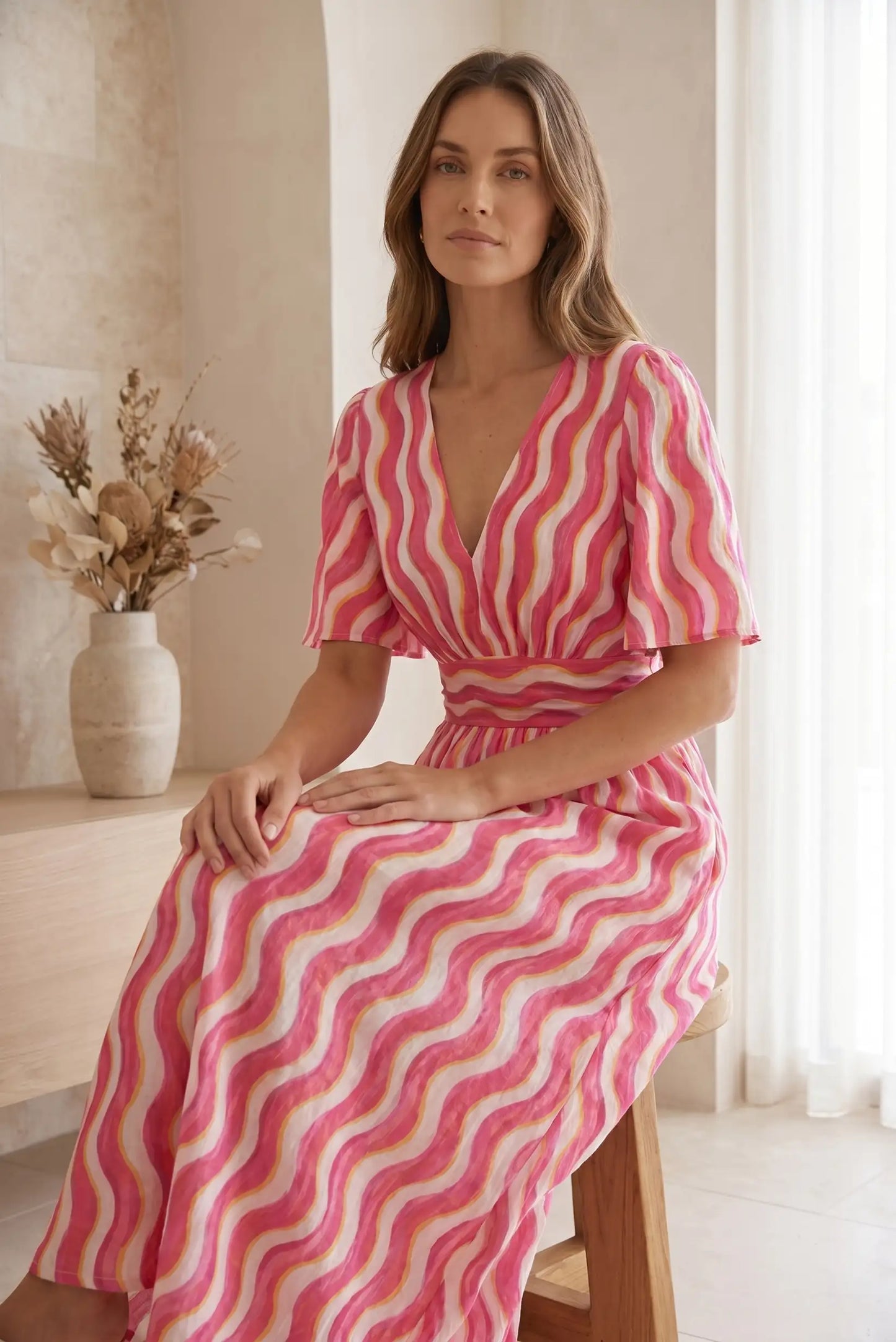 Mujer con vestido largo estampado de rayas onduladas rosas, sentada en interior luminoso.