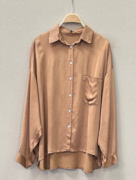 camisa satinada beige manga larga con bolsillo, colgada en percha sobre fondo neutro