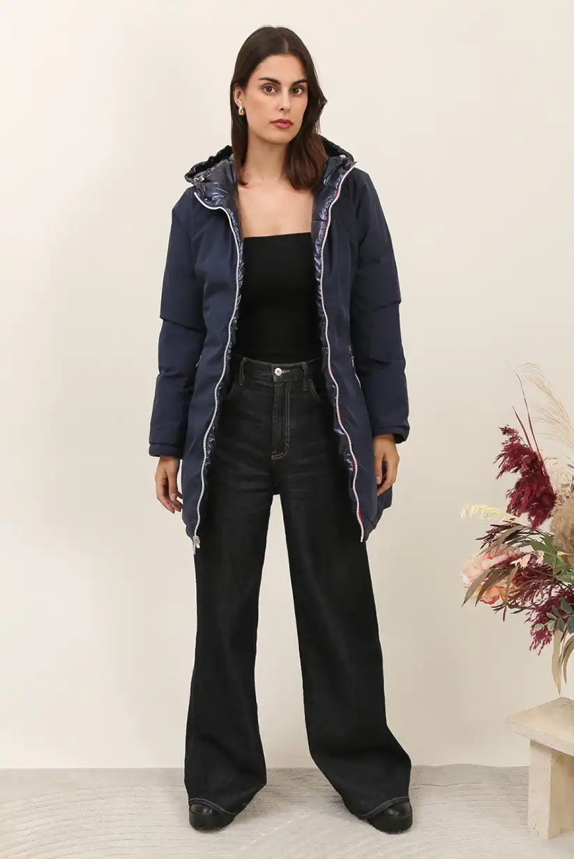 Mujer con abrigo largo azul reversible de invierno y pantalón negro, fondo beige.