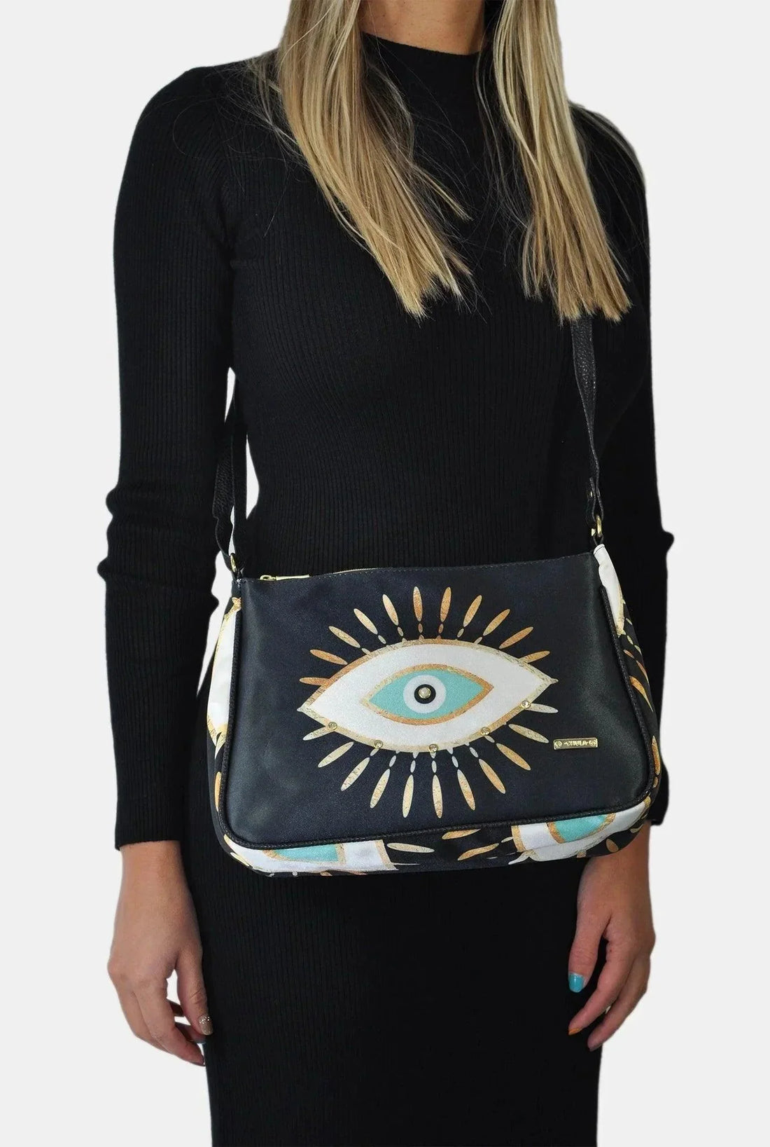 Mujer con bolso bandolera mediano negro, diseño ojo turco dorado, vestido negro.