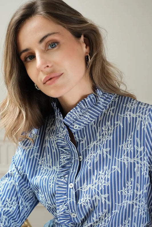 Mujer con camisa azul de rayas y bordados florales blancos, moda femenina elegante.