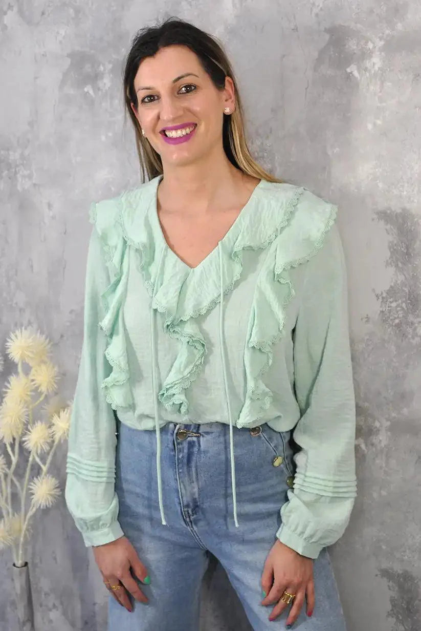 Mujer con camisa verde agua con volantes y jeans, fondo gris, moda primavera verano 2025