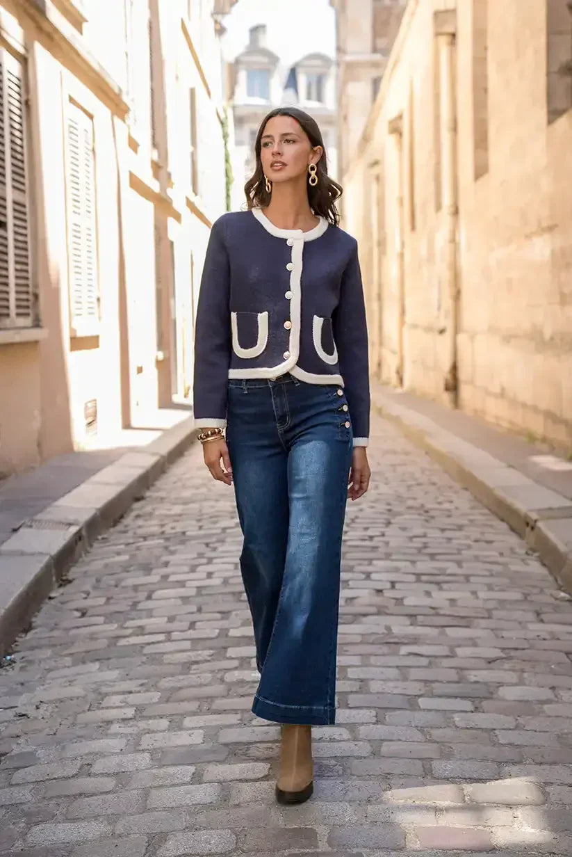 Mujer con chaqueta azul marino beige y jeans anchos caminando por calle empedrada