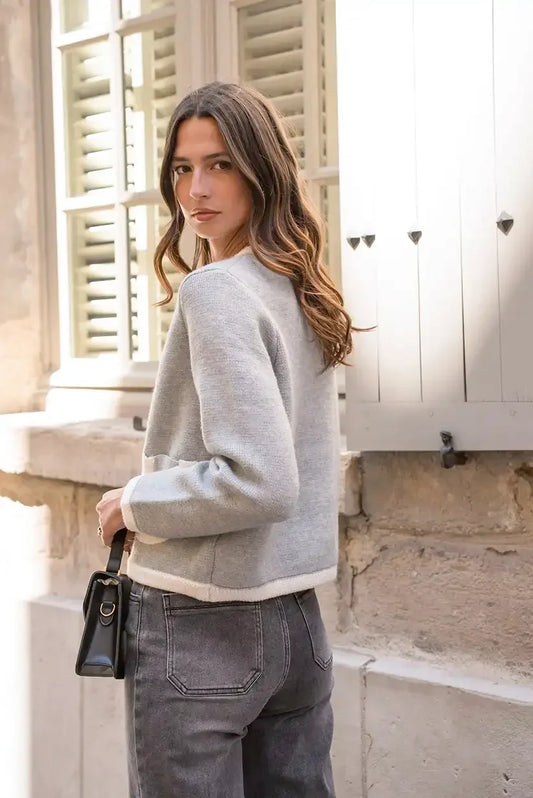 Mujer con chaqueta gris beige y bolso negro, de espaldas en calle urbana iluminada.