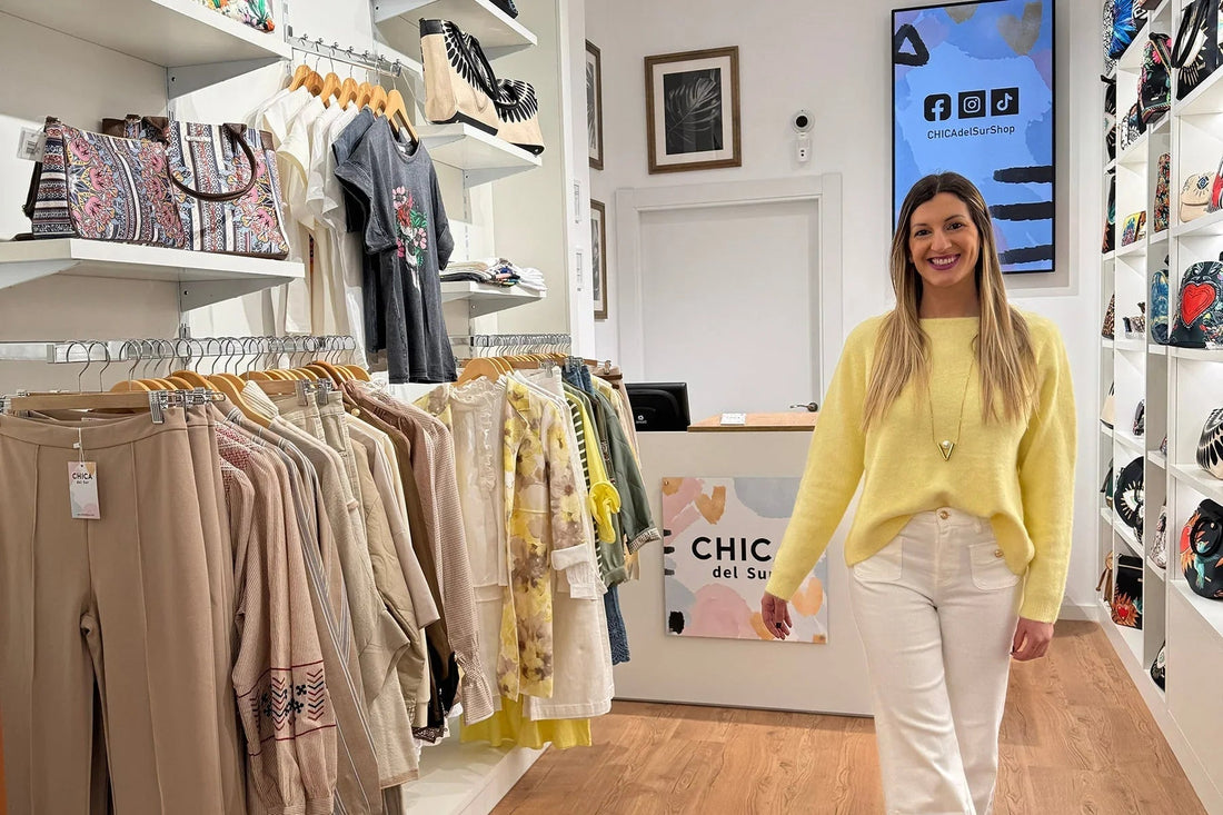 Mujer joven sonriente en tienda de moda Chica del Sur, con ropa y bolsos en exhibición.
