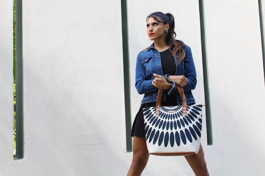Mujer con bolso estampado en blanco y negro, chaqueta de mezclilla y vestido negro frente a pared blanca