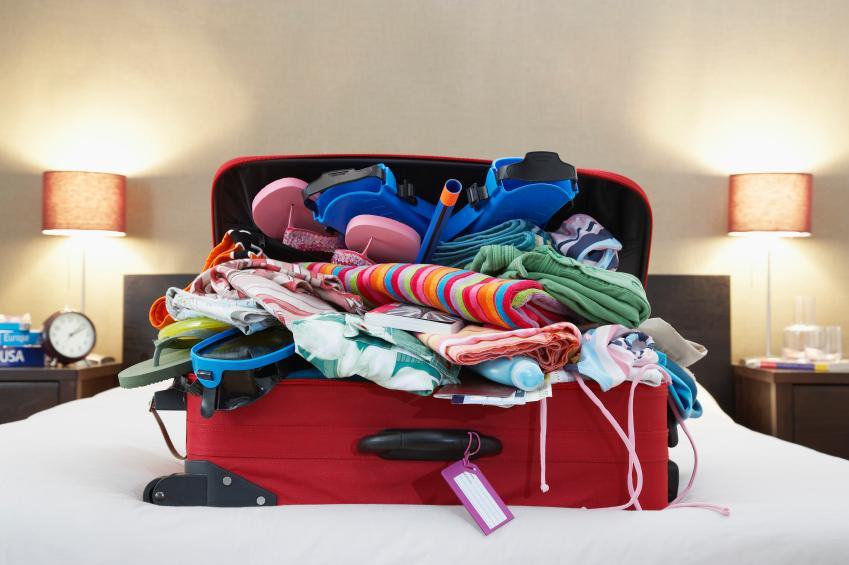 Maleta roja sobre cama, ropa colorida desbordada, tips de viaje y organización de equipaje