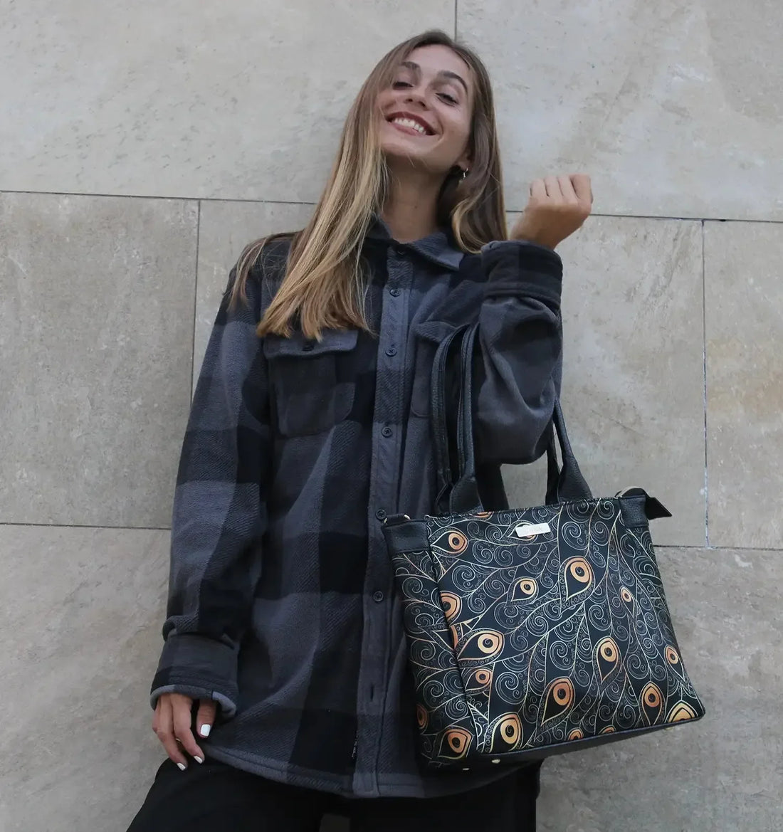 Mujer joven sonriendo con bolso de diseño elegante y chaqueta a cuadros frente a pared beige