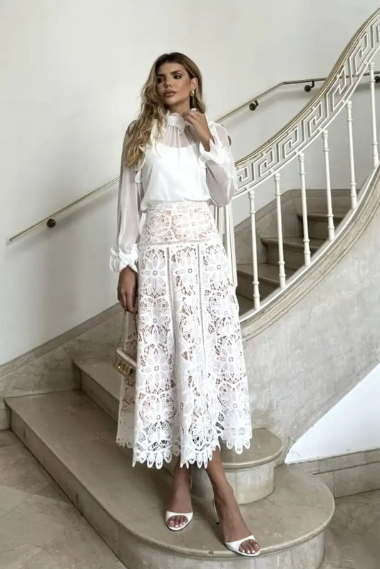 Mujer con falda midi blanca de encaje floral y blusa blanca en escaleras elegantes