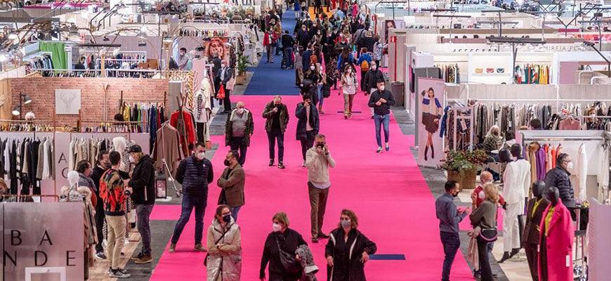 Personas recorren una feria de moda en España con stands de ropa y alfombra rosa