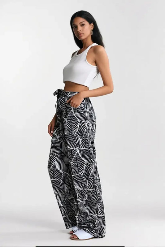 Mujer con pantalón fluido largo blanco y negro de hojas y top blanco, fondo neutro