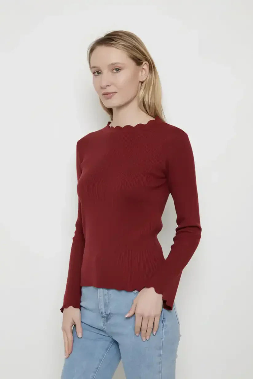 Mujer con camiseta burdeos de manga larga y detalles ondulados, combinada con jeans claros, fondo blanco