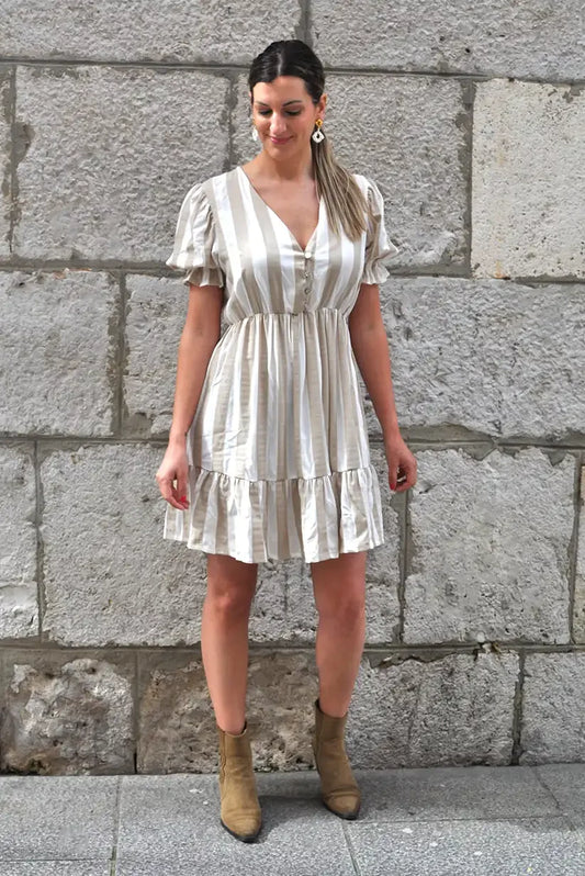 Mujer con vestido corto primavera de rayas beige y blanco, tendencia 2025, fondo de piedra